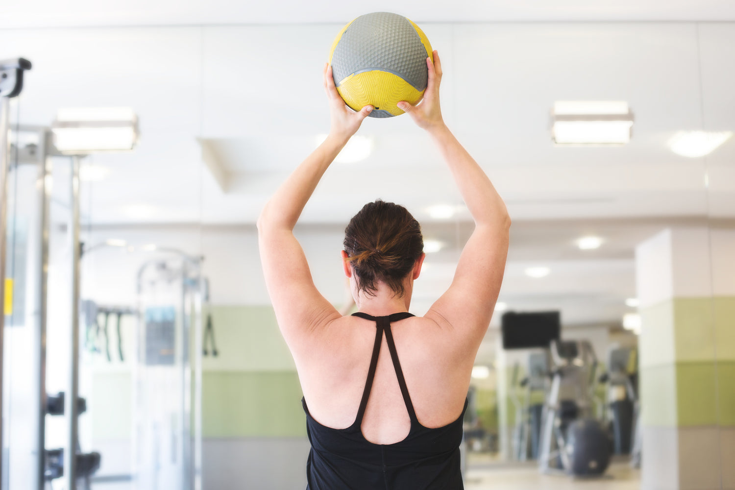 the back of a women in the gym holding a ball above her head